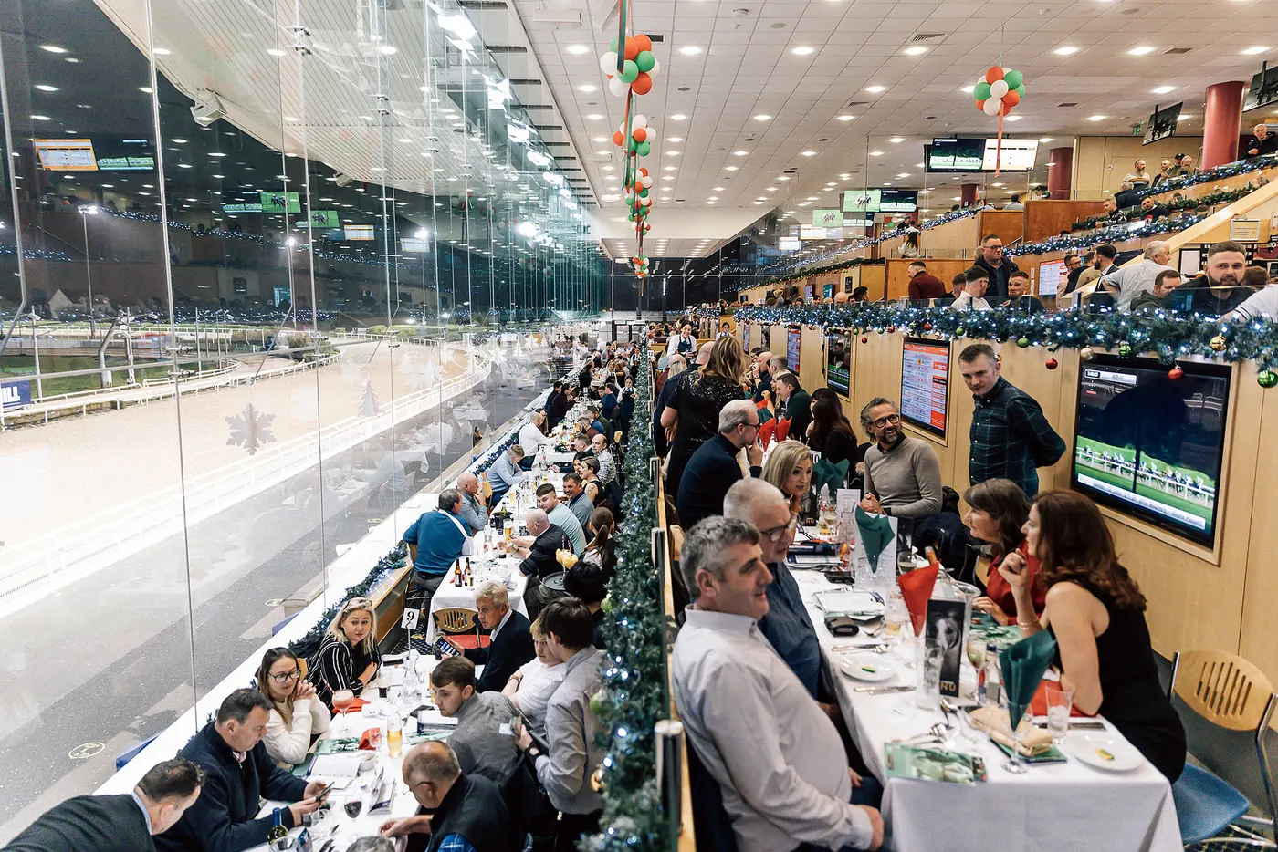 A long table of guests at a Christmas party night in The View, garlands along the glass.